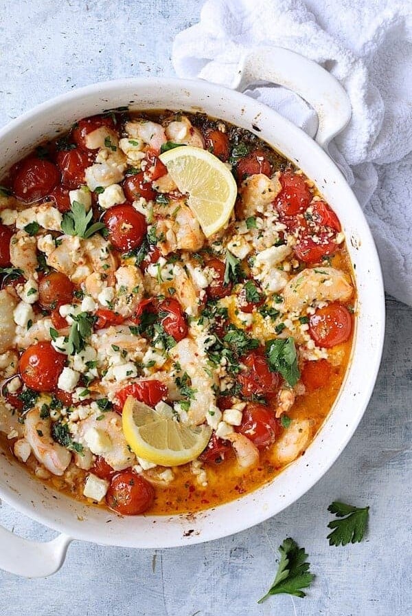 Spicy Baked Shrimp with Tomatoes and Feta Cheese in round white baking dish garnished with parsley and lemon.