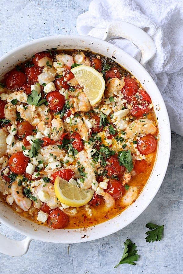 Photo of Spicy Baked Shrimp with Tomatoes and Feta Cheese on pale blue background.