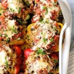 Chicken, Rice and Black Bean Stuffed Peppers in white baking dish with white serving spoon.