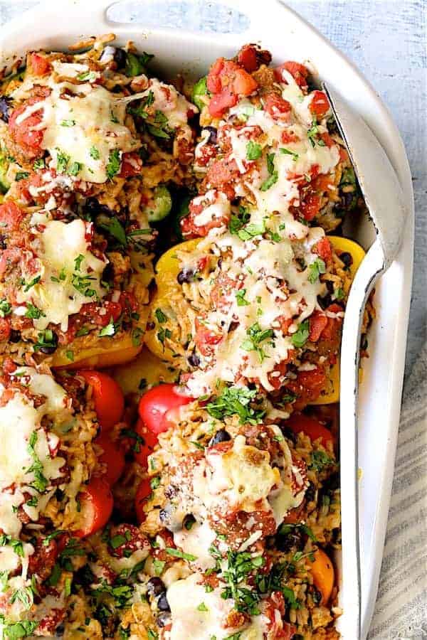 Close-up photo of Chicken, Rice and Black Bean Stuffed Peppers in white baking dish with white serving spoon.