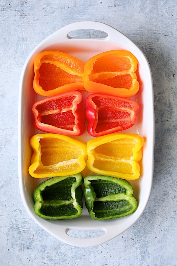 Photo of four peppers cut in half in white baking dish to form eight halves.