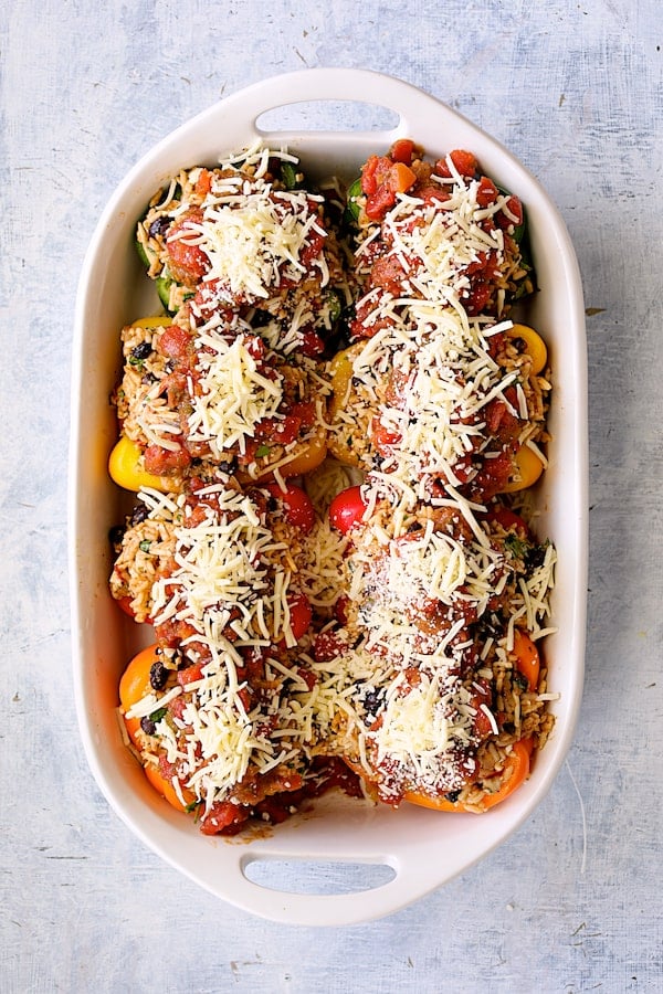 Photo of assembled peppers in white baking dish with salsa and cheese added.