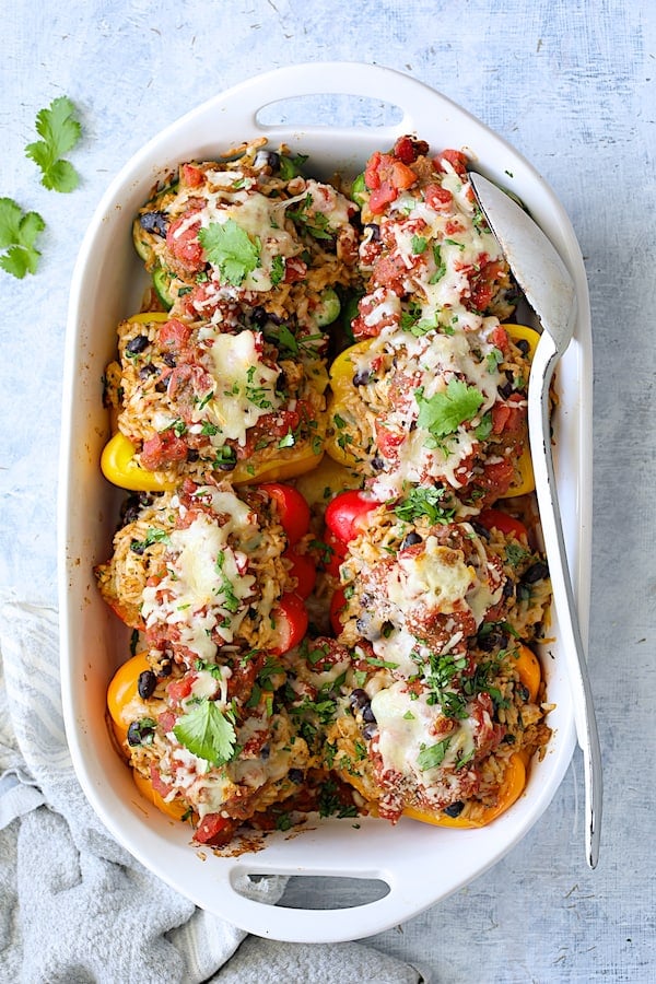 Photo of eight Chicken, Rice and Black Bean Stuffed Peppers in white baking dish after being baked with white serving spoon.