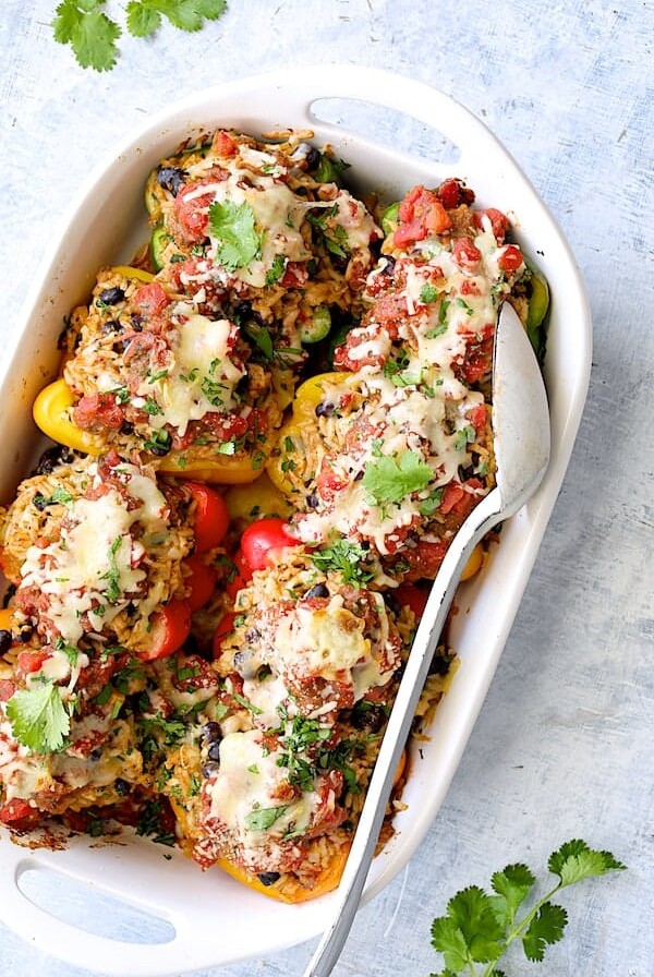Eight Chicken, Rice and Black Bean Stuffed Peppers in white baking dish with white serving spoon after being baked.