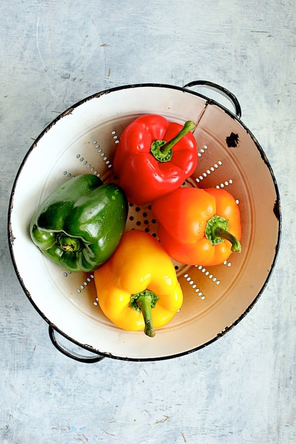 Photo of four bell peppers in various colors in white vintage colander.