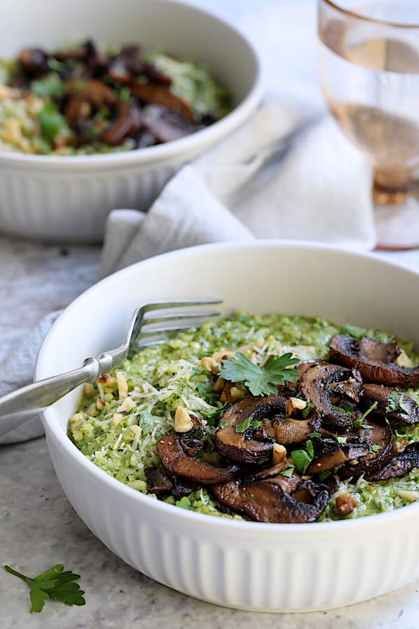 Photo of two bowls of Oven Risotto with Kale Pesto and Roasted Mushrooms garnished with fresh parsley.