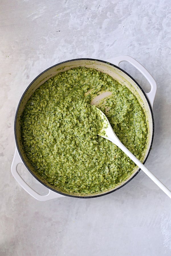 Photo of finished risotto in white cast iron pan after adding pesto being stirred with white spoon.