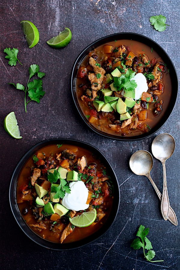 Slow Cooker Southwestern Turkey, Butternut Squash and Black Bean Stew - Overhead shot of two bowls of the stew garnished with avocado, cilantro and lime