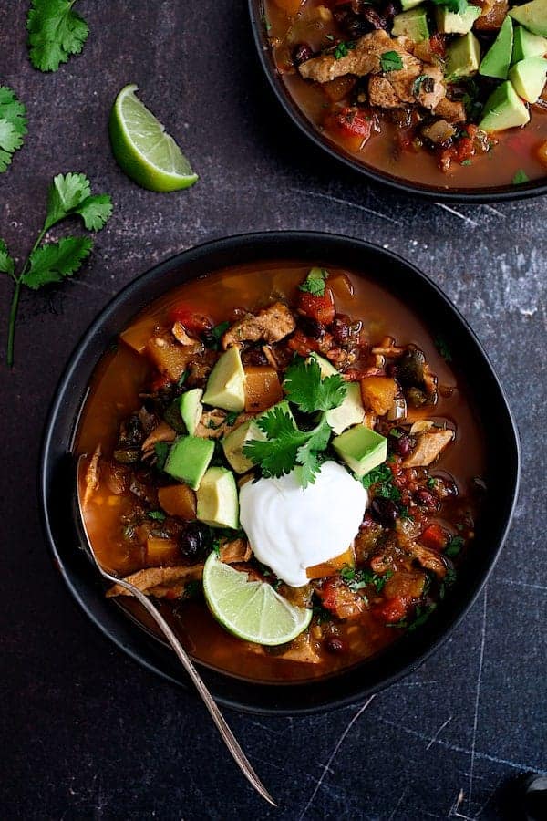 Slow Cooker Southwestern Turkey, Butternut Squash and Black Bean Stew - Overhead hero shot in black bowls garnished with avocado, sour cream and lime