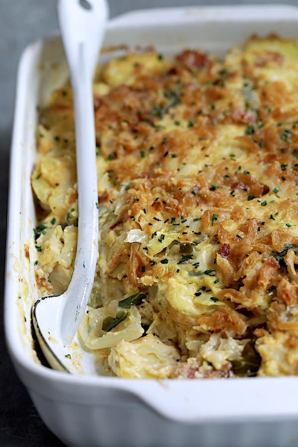 Potato and Cabbage Casserole with Cheddar and Bacon with some spooned out with white serving spoon on the side.