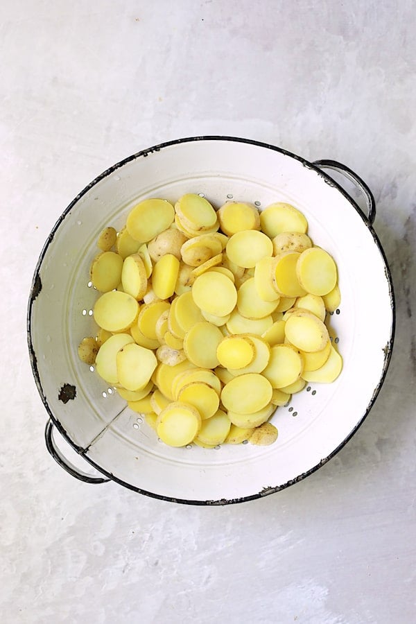 Photo of sliced cooked baby Yukon gold potatoes in vintage white colander.