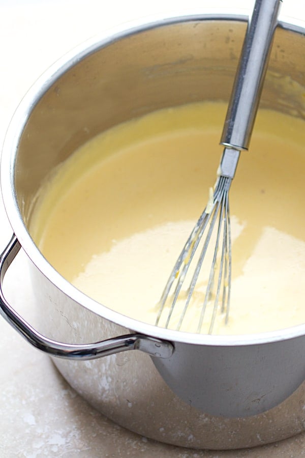 Photo of cheese sauce in stainless steel saucepan with whisk.