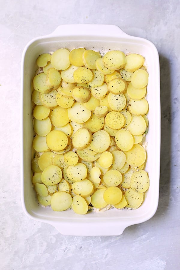Photo of first layer of potatoes placed over cabbage in white rectangular baking dish.