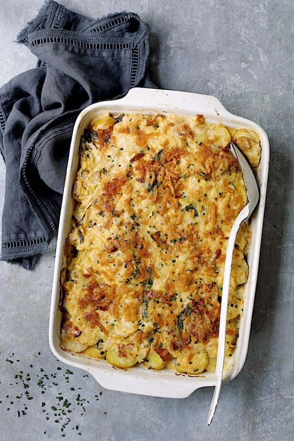 Potato and Cabbage Casserole with Cheddar and Bacon on blue background with blue towel garnished with fresh chives.