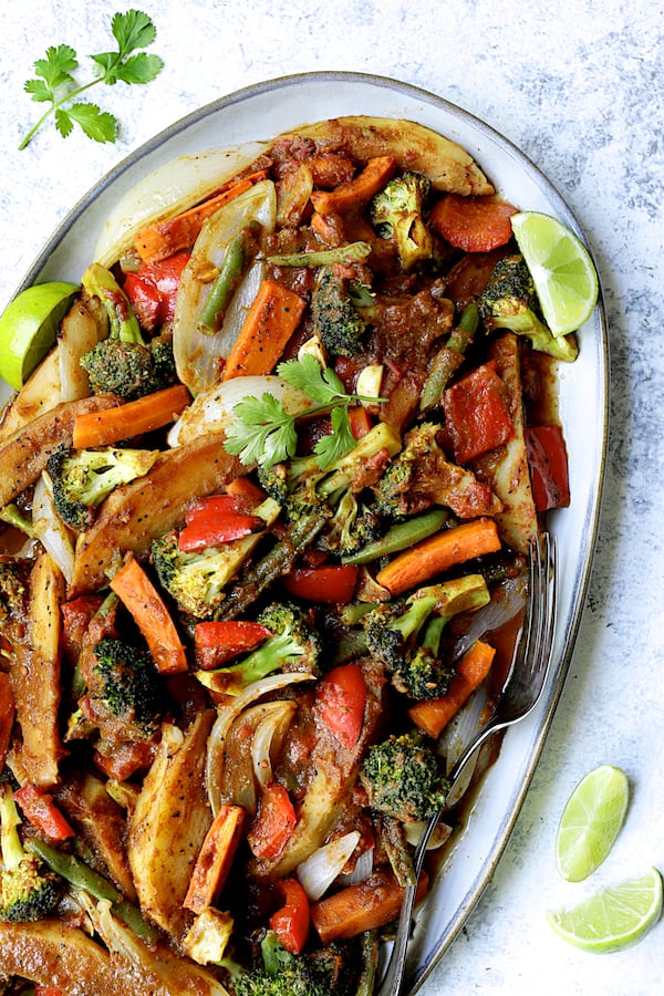 Photo of Curried Roast Vegetables on oval platter with lime wedges and cilantro sprigs.