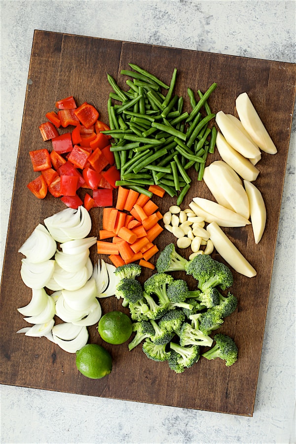 Photo of red bell pepper, green beans potatoes, carrots, onions, garlic, broccoli and limes.