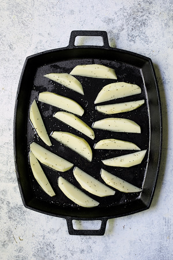Photo of uncooked potato wedges on cast iron pan.