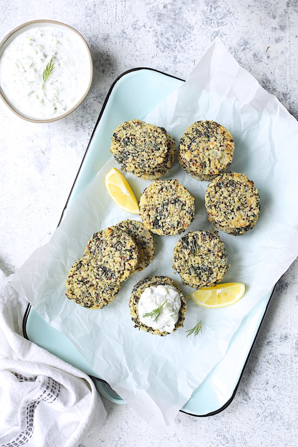 Photo of Greek Quinoa Cakes with Tzatziki on parchment paper-lined light blue platter with lemon wedges.