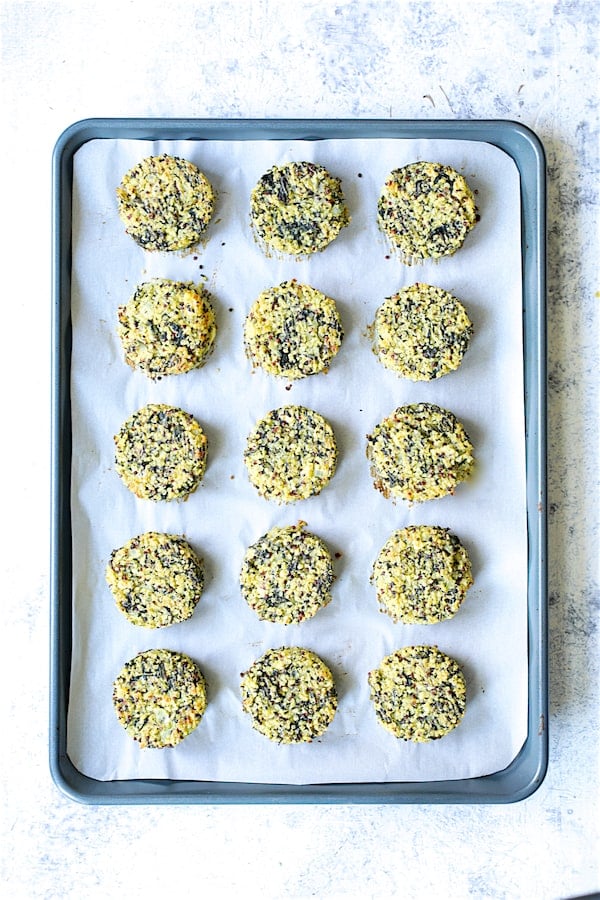 Photo of 15 baked Greek Quinoa Cakes with Tzatziki on parchment paper-lined baking sheet.