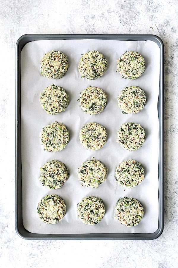 Photo of 15 quinoa cakes on parchment paper-lined baking sheet before being baked.