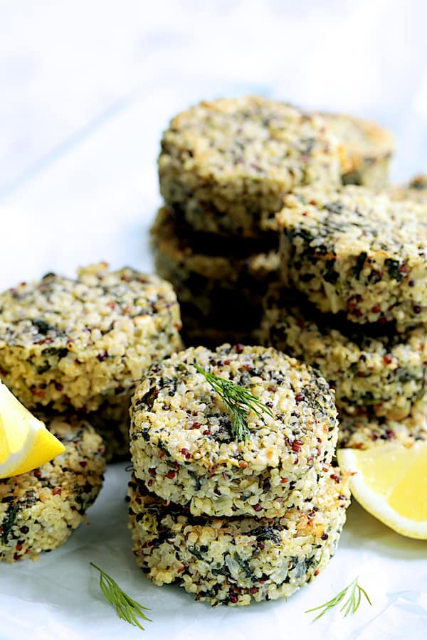 Close-up photo of Greek Quinoa Cakes stacked with lemon wedges and dill sprigs.