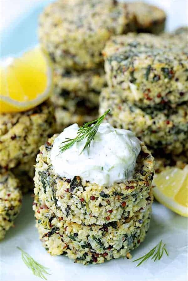 Two Greek Quinoa Cakes with Tzatziki stacked with tzatziki, garnished with lemon wedges and dill sprigs.