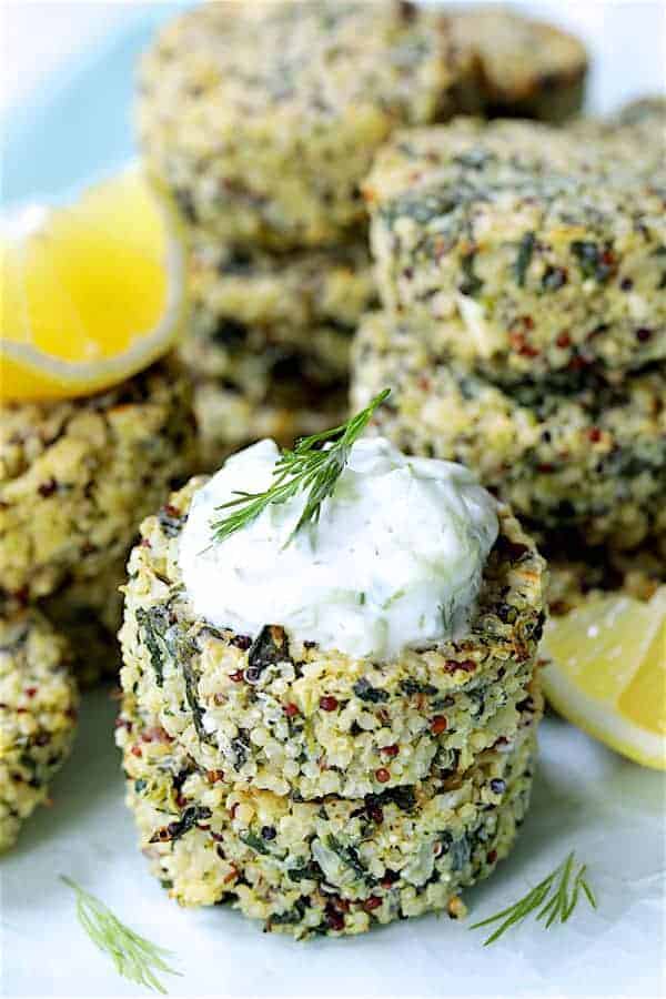 Close-up photo of two stacked Greek Quinoa Cakes with Tzatziki garnished with lemon wedges and dill sprigs.