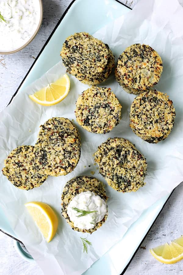 Photo of Greek Quinoa Cakes with Tzatziki on parchment paper-lined platter garnished with lemon wedges.