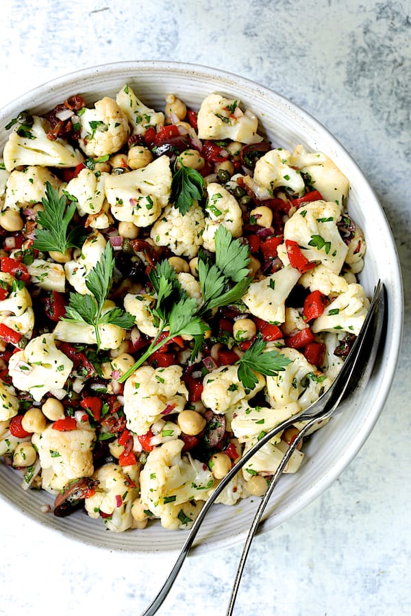 Close-up photo of Sicilian Cauliflower Salad in white serving bowl garnished with parsley sprigs.