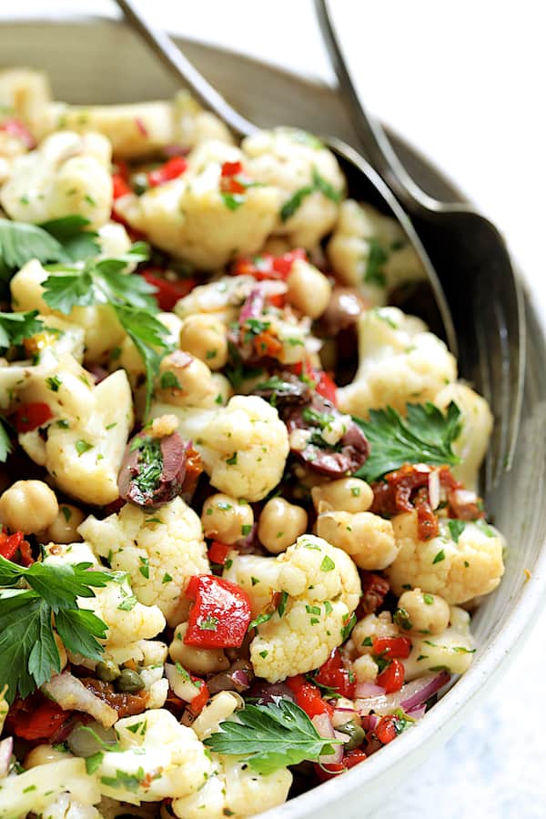 Close-up photo of Sicilian Cauliflower Salad in white serving bowl with serving utensils.