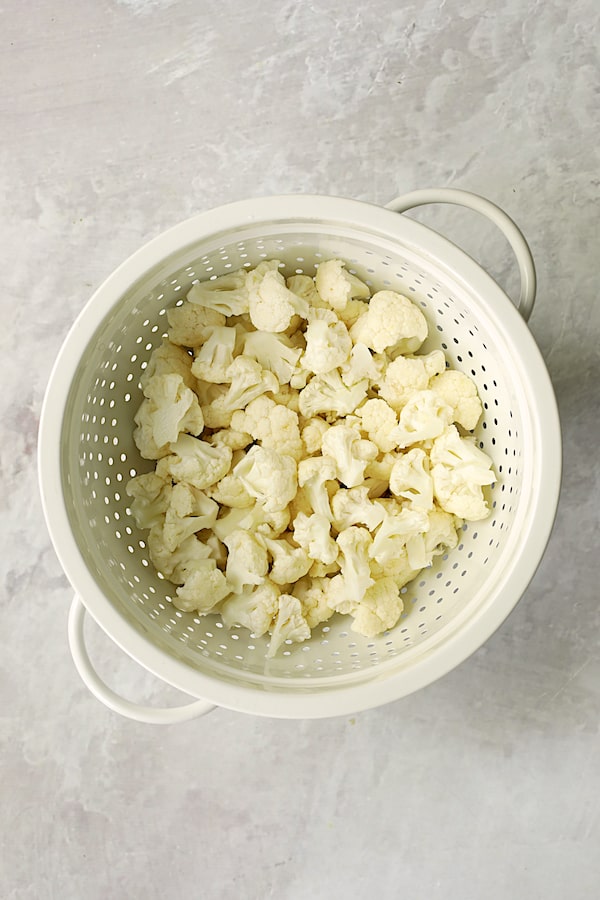 Photo uncooked cauliflower florets in white colander.