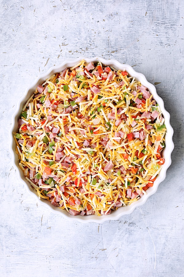 Photo of peppers, ham and cheese in round white baking dish before custard is poured in.