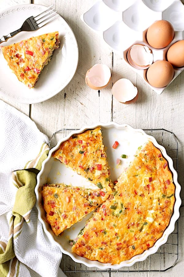 Photo of Spicy Baked Denver Omelet on white distressed wood background with slices removed.