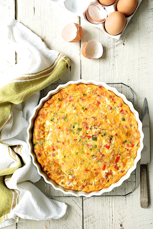 Photo of cooked Spicy Baked Denver Omelet on cooling rack with green striped towel and egg shells nearby.