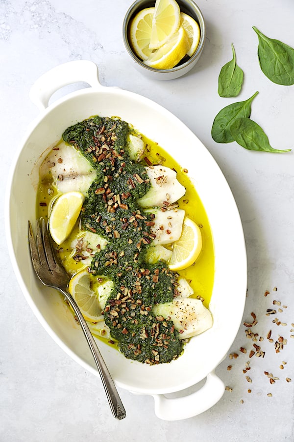 Photo of Baked Tilapia with Spinach Pecan Pesto in white baking dish with serving fork.