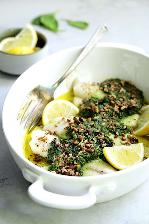 Photo of Baked Tilapia with Spinach Pecan Pesto in white baking dish with serving fork.
