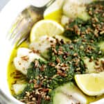 Baked Tilapia with Spinach Pecan Pesto - Straight-on close-up shot of finished dish garnished with chopped pecans and lemon wedges