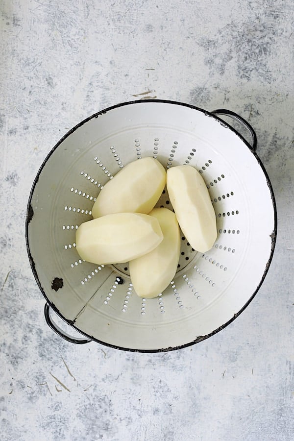 Photo of four peeled Russet potatoes in antique white colander.