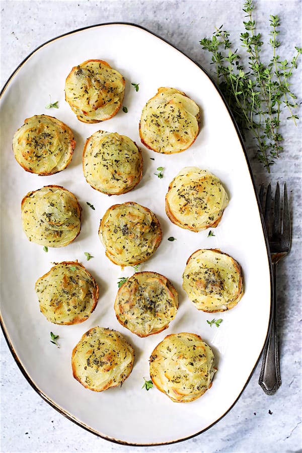 Photo of Garlic Herb Muffin Pan Potato Galettes on white oval platter garnished with fresh thyme.