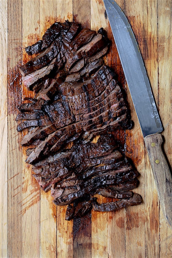 Photo of sliced skirt steak on wood cutting board with butcher knife.