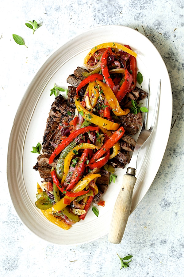Photo of Grilled Marinated Skirt Steak with Peperonata on white oval platter with meat fork.