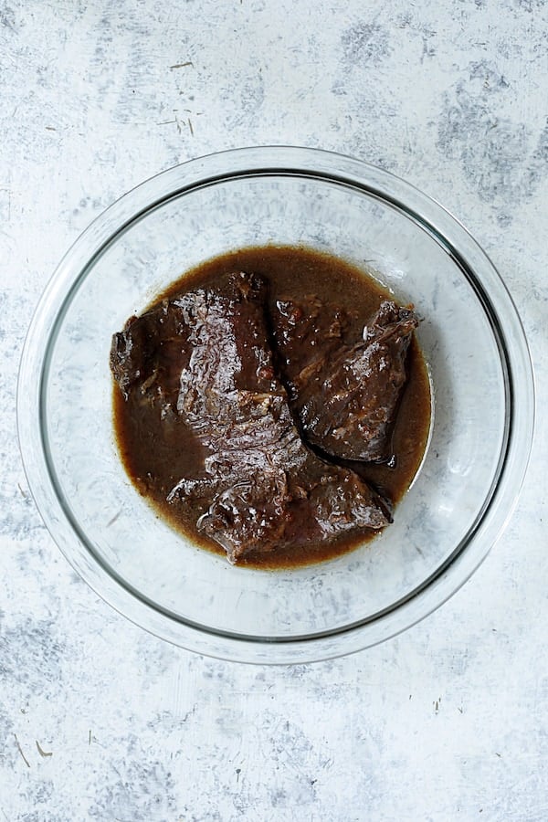 Photo of skirt steak marinating in glass bowl.