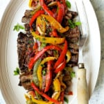 Grilled Marinated Skirt Steak with Peperonata on white oval platter with meat fork.