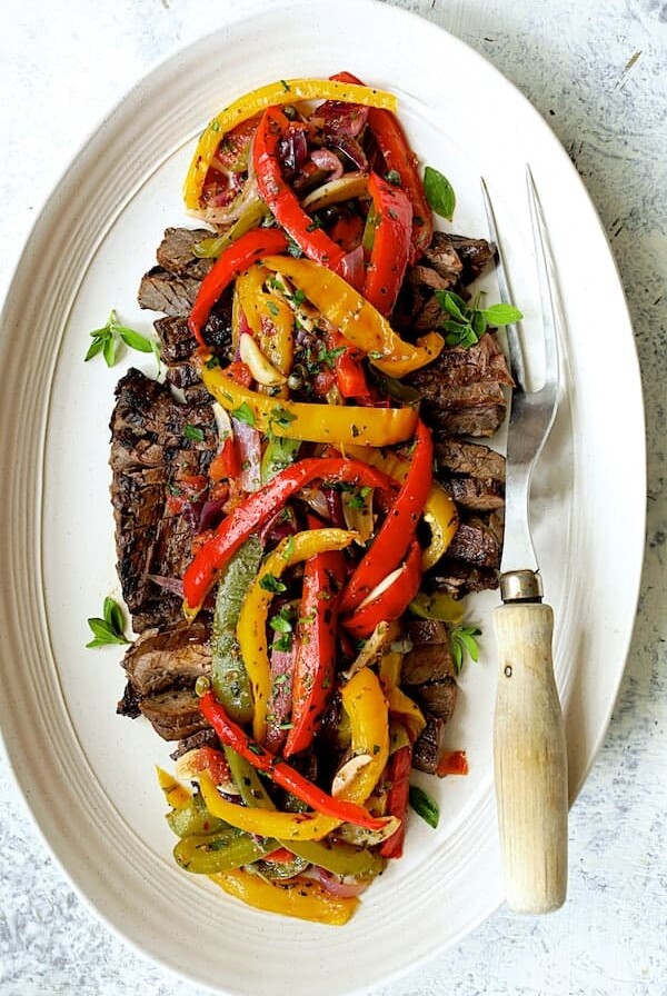 Grilled Marinated Skirt Steak with Peperonata on white oval platter with meat fork.