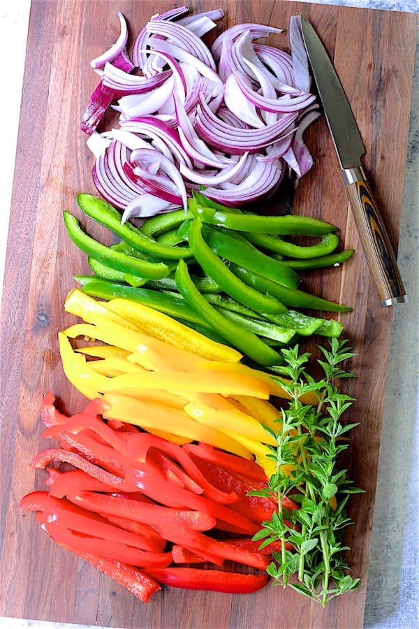 Photo of multicolored peppers and onions on wood cutting board.