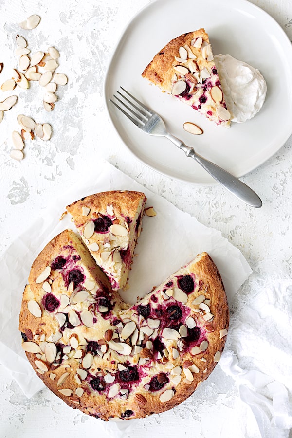 Photo of Raspberry Ricotta Cake with Almonds on white background with a wedge on white plate with whipped cream.