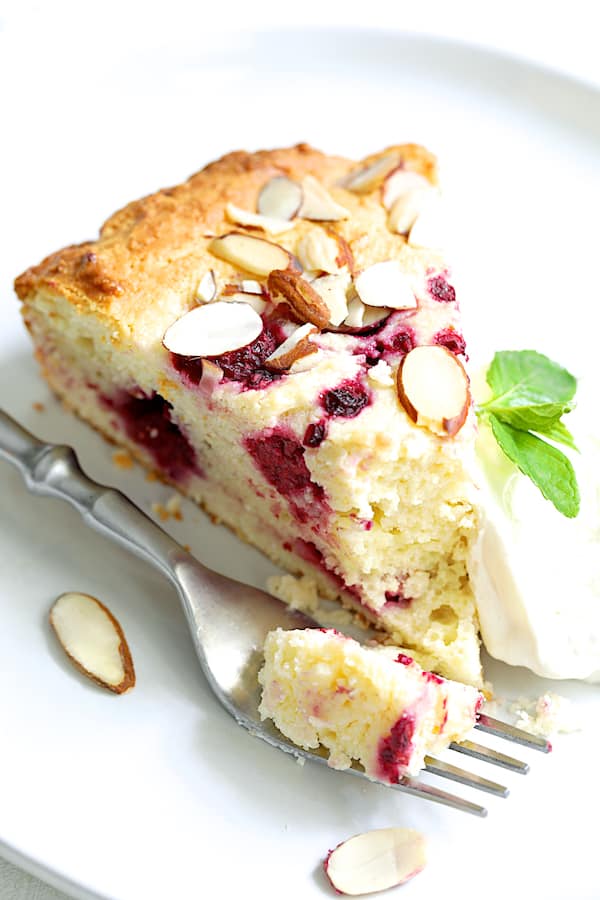 Close-up photo of a piece of Raspberry Ricotta Cake with Almonds on white plate with some on a fork.