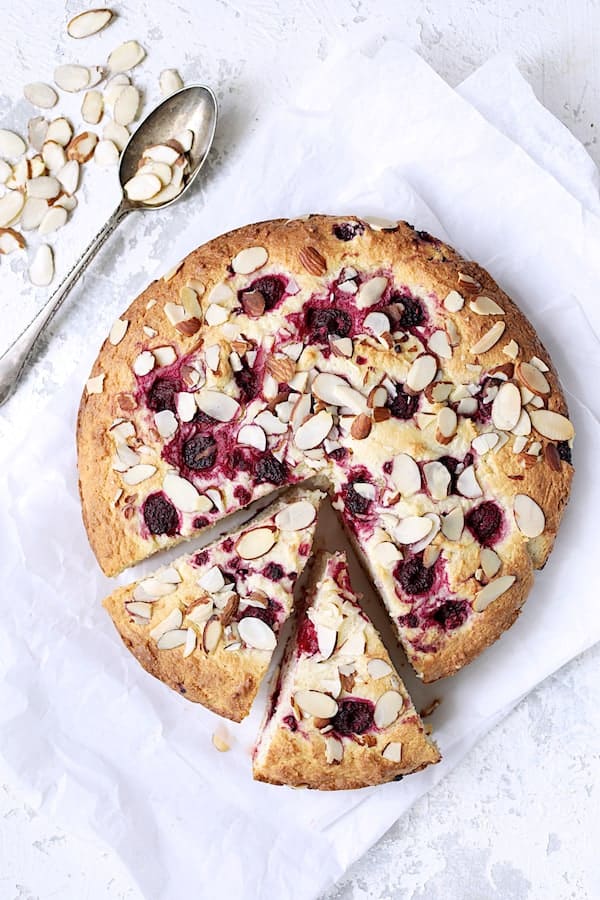 Photo of Raspberry Ricotta Cake with Almonds on white paper with two pieces cut into it and almonds scattered about.