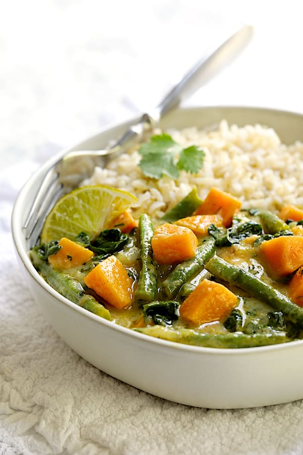 Photo of a bowl of Vegan Thai Green Sweet Potato Curry with rice on white fabric.