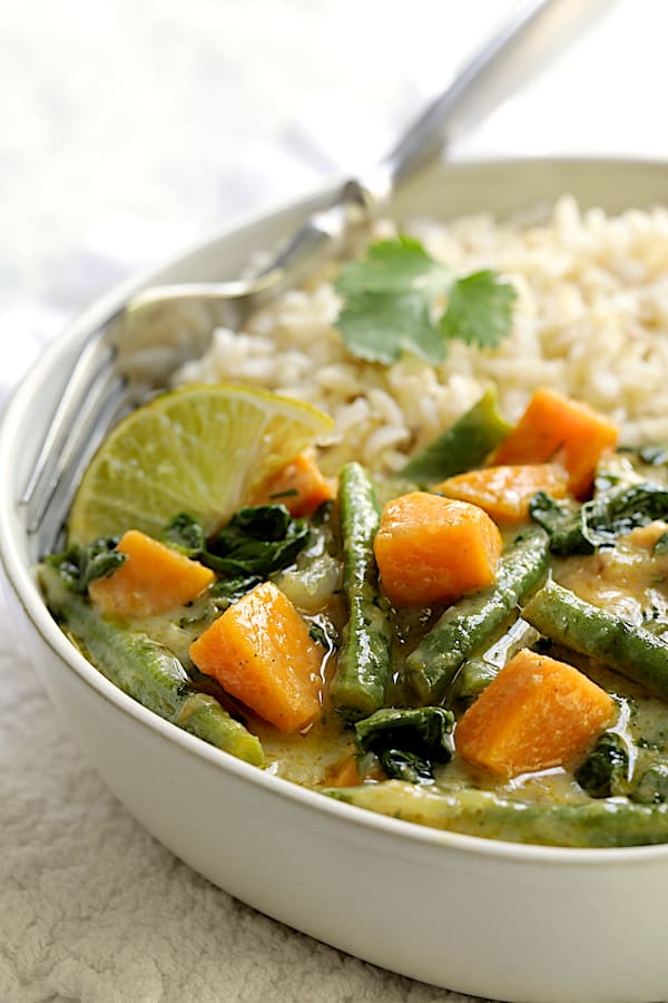 Close-up photo of Vegan Thai Green Sweet Potato Curry in white bowl with rice and fork.